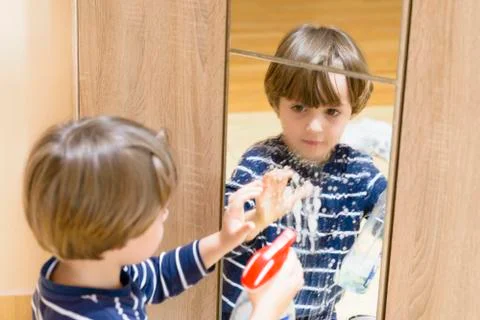 Cute boy cleaning the mirror using some spray Stock Photos