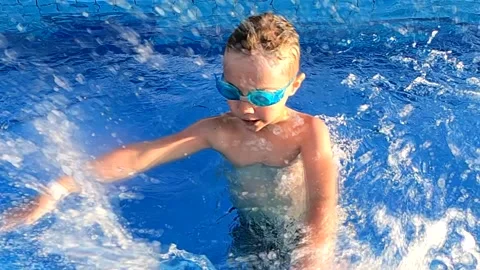 Cute boy creates a lot of splashes in the pool, enjoying water treatments on a Stock Footage 171207153