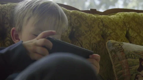Cute boy curls up on a couch and plays on a phone Stock Footage 64643800