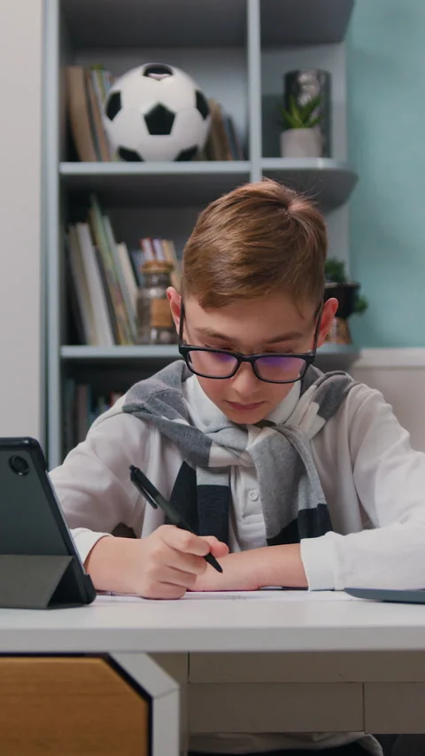 Cute boy is doing homework at table with laptop at home. Kid enjoys making schoo Stock Footage 329889666