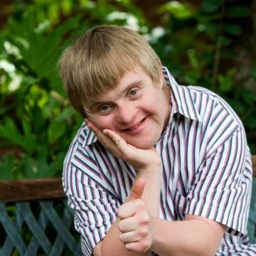 Cute boy with down syndrome doing thumbs up in garden. Foto stock