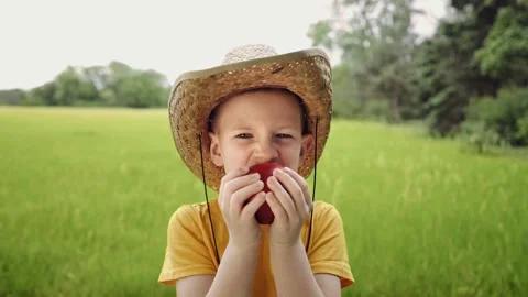 Cute boy eating a big red apple. Kid from the countryside in a straw hat. Stock-Footage 149240850