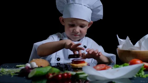 Cute boy is eating a burger while cooking. He wears chefs suit and cap. Stock Footage 92559734