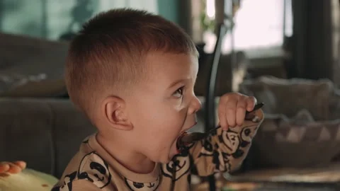 Cute boy eating chocolate pudding with dirty face at home in living room. Stock Footage 165847389