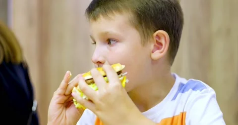 Cute boy eating large hamburger at fast food restaurant. Unhealthy meal for k Stock Footage 170023324