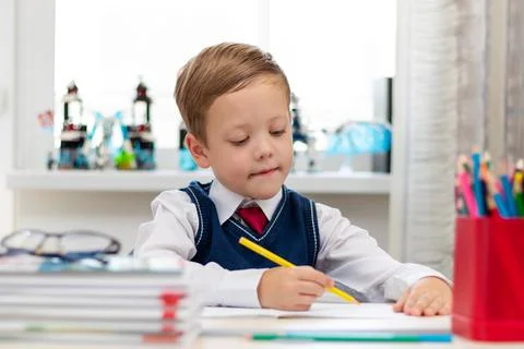 A cute boy first grader in a school uniform does homework while sitting at a  Stock Photos