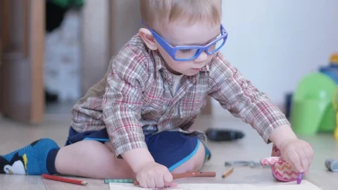Cute boy in funny glasses draws with both hands on paper at home Stock Footage 88961388