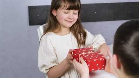 A cute boy gives a dark-haired cute girl a gift box. Stock Footage 146788755