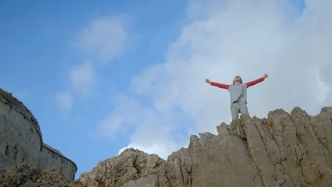 Cute boy in a gray jacket with red sleeves stands  on a cliff Stock Footage 100827890