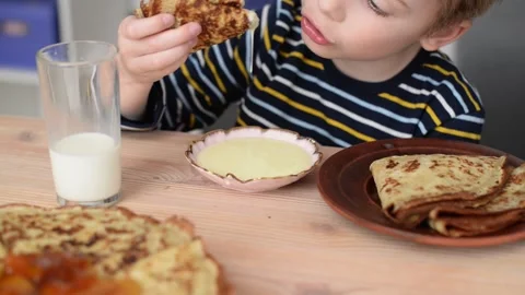 A cute boy has breakfast, eats pancakes, dips them in condensed milk, close-up Stock Footage 194566123