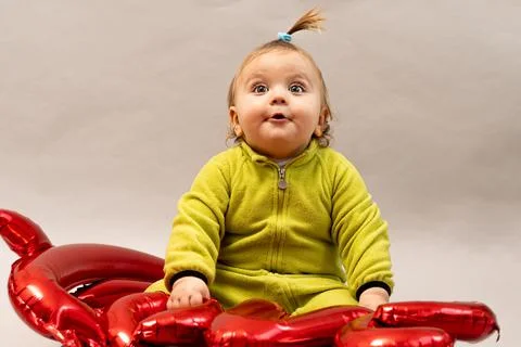 Cute boy having fun with red balloon in green clothes on gray background Stock Photos