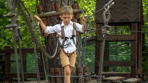 Cute boy having fun while walking on wobbly rope bridge at adventure park. .. Foto stock