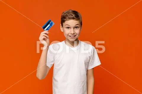 Cute boy holding credit card, orange studio background Stock Photos