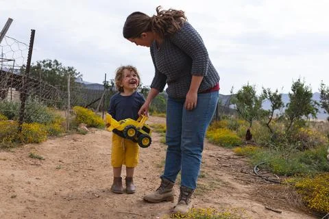 Cute boy holding toy bulldozer while standing with mother on walkway at organic Stock Photos