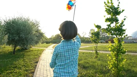 Cute boy holding toy wind turbine in hand, running at sunset summer park. Happy Stock Footage 99890448