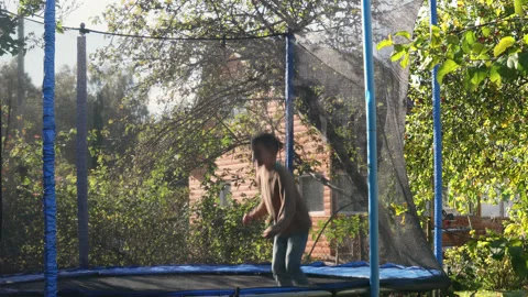Cute boy jumping on trampoline and doing somersault in the garden in the sunset Stock Footage 215526227