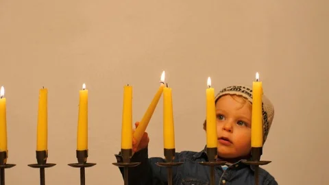 Cute boy in kippa keeps candle and inflaming candle on menorah Stock Footage 104555502