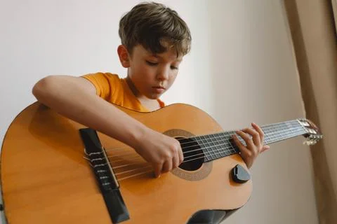 Cute boy learns to play the classical guitar in home. Cozy home. Stock Photos