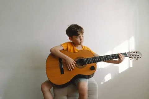 Cute boy learns to play the classical guitar in home. Cozy home. Stock Photos