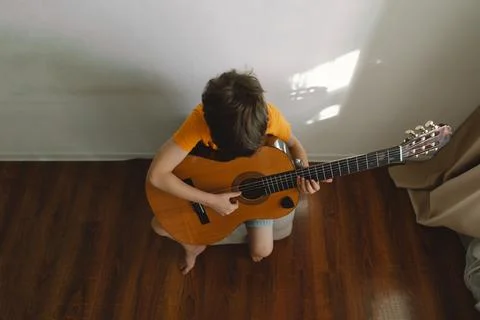 Cute boy learns to play the classical guitar in home. Cozy home. Stock Photos