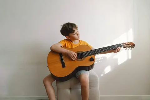Cute boy learns to play the classical guitar in home. Cozy home. Stock Photos