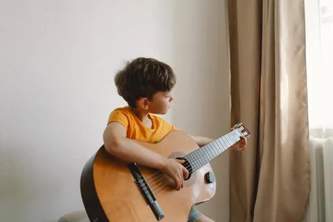Cute boy learns to play the classical guitar in home. Cozy home. Stock Photos