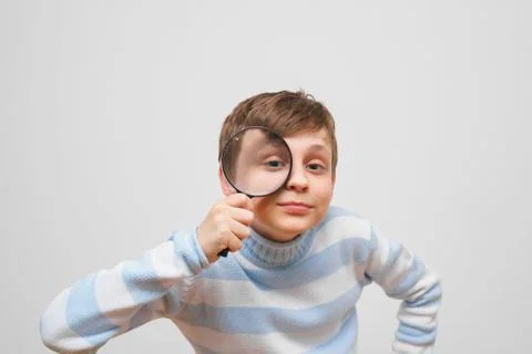 Cute boy looking at camera through magnifying glass, on white ba Stock Photos