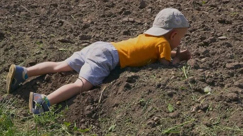 Cute boy lying on dusty ground playing and swinging legs in sunny day Stock-Footage 77095796
