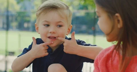 Cute boy makes funny faces in front of his sister in park Stock Footage 116117028