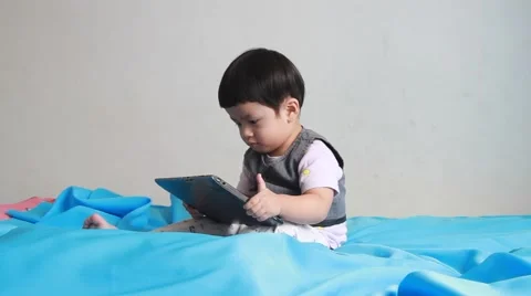 Cute boy play tablets on the bed. Stockbeeldmateriaal 55424210