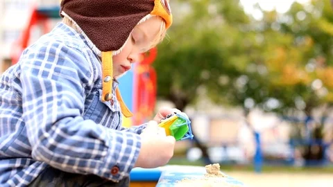 Cute boy playing in sandbox outside in modern fashionable kids clothes on Vidéo 119054489