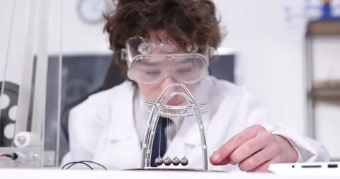 Cute boy plays with a Newton's Cradle. A young boy dragging a small metal ball Stock Footage 172199473