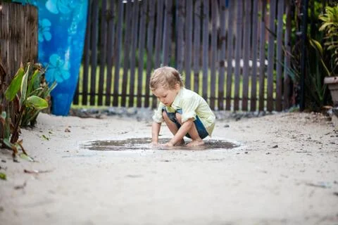 Cute boy plunging hands in puddle and watching water Stock Photos