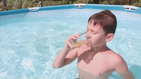 Cute boy in the pool drinks a refreshing drink, the sun is shining. Stock Footage 248376639