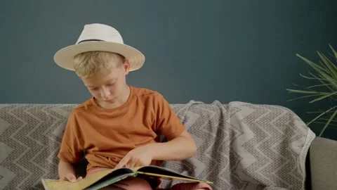 A cute boy is reading a book sitting on the couch at home. the child spends time Stock Footage 158855974