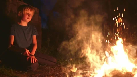 Cute boy is roasting marshmallows on a bonfire on a summer evening Stock Footage 329598635
