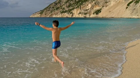 Cute boy running through the water at the beach with turquoise water Stock Footage 97933114