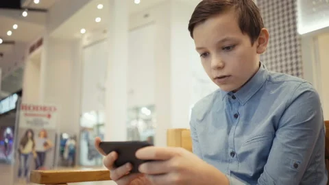 Cute boy sits on the bench in the mole hall and plays emotionally in a game on Stock Footage 97850336