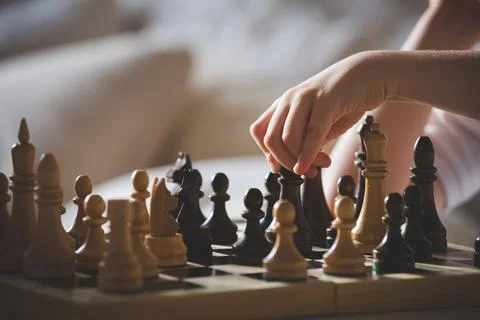 Cute boy sits at a table and plays chess. The kid picked up the chess piece Stock Photos