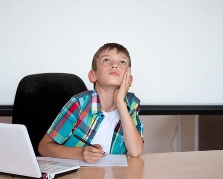 A cute boy sits at the table, looks up, remembers his homework. The boy didn' Stock Photos