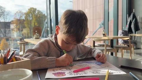 Cute boy sitting in the cafe and coloring Stock Footage 277595410