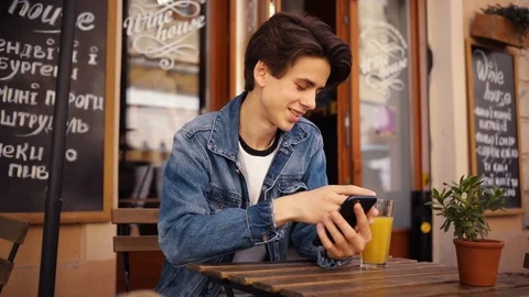 Cute boy sitting in cafe use phone drink juice smile feel happy outdoor guy Stock Footage 92052546