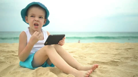 Cute boy sitting at sandy beach and using smartphone app Stock Footage 106518362