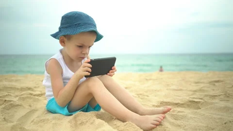 Cute boy sitting at sandy beach and using smartphone app Stock Footage 107146373
