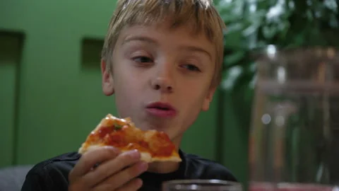 Cute boy taking big bite of cheese pizza at restaurant. Hungry kid boy eating Stock Footage 168987840