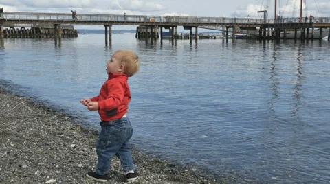 Cute boy throws rocks in water pier in background Stock Footage 67881603