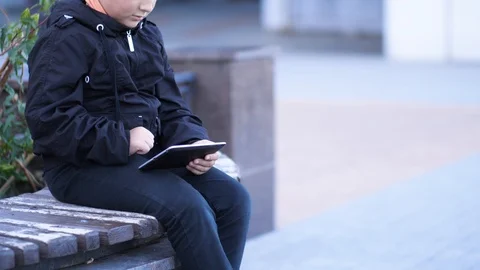 Cute boy uses a tablet on a bench in the park Stock Footage 96588353