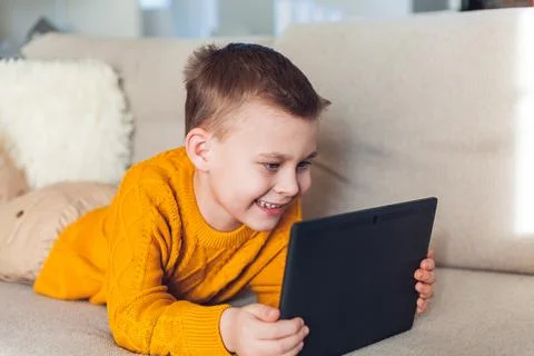 Cute boy uses a tablet. The boy speaks by video link. Quarantine. Stock Photos
