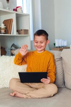 Cute boy uses a tablet. The boy speaks by video link. Quarantine. Stock Photos