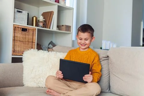 Cute boy uses a tablet. The boy speaks by video link. Quarantine. Stock Photos